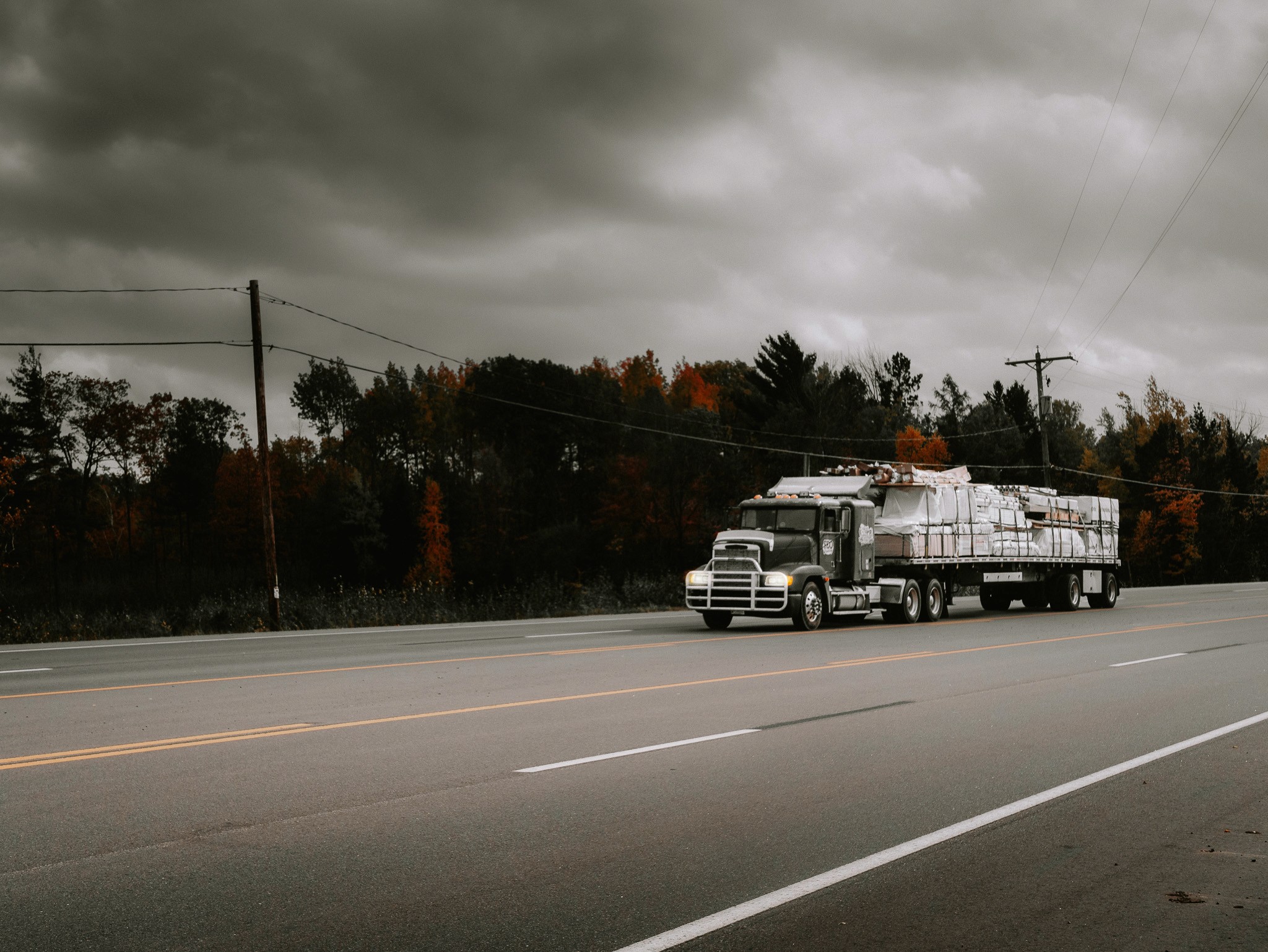 A flatbed truck traveling along a tree-lined road